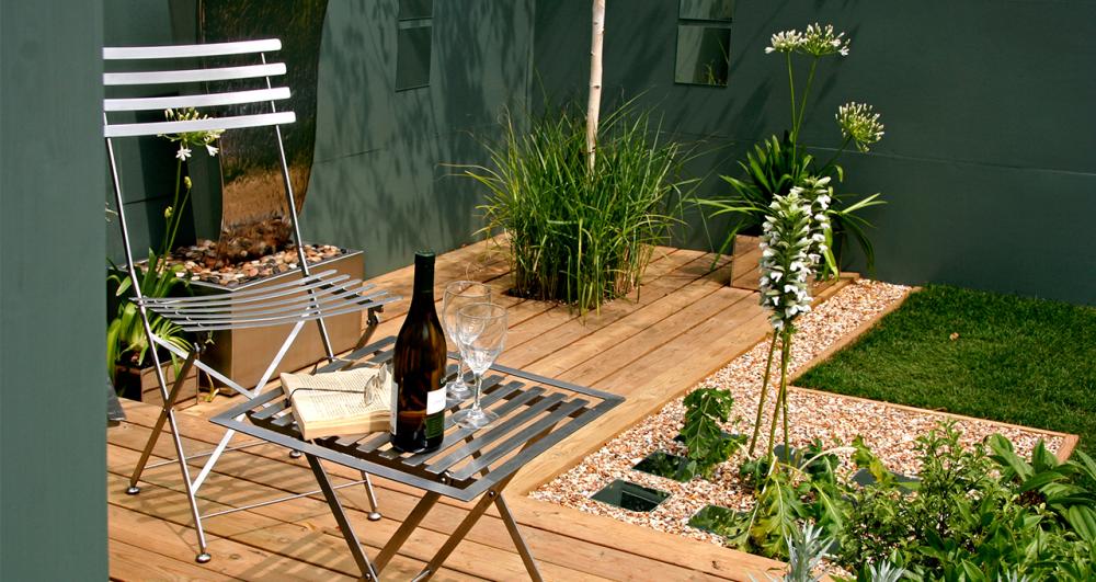a decked patio with a chair and table surrounded by gravel flower beds and a lawn