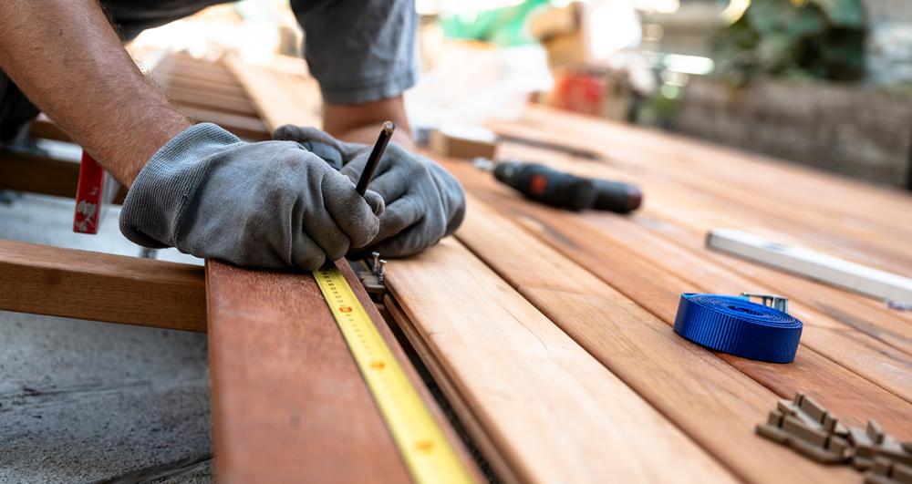 a homeowner in the process of installing garden decking measuring up the timber boards