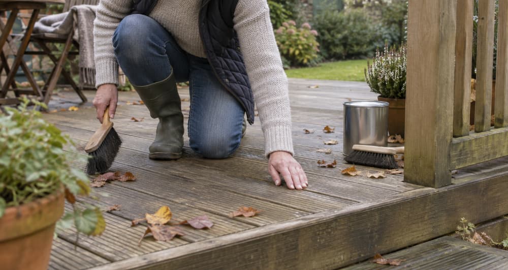 Homeowner clearing fallen leaves from timber garden decking