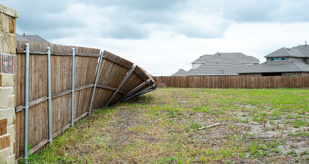 Leaning wooden garden fence panels damaged by strong wind in a backyard.