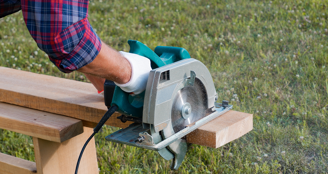 A close-up on gloved hands holding a circular saw as a DIYer cuts timber for a garden bar