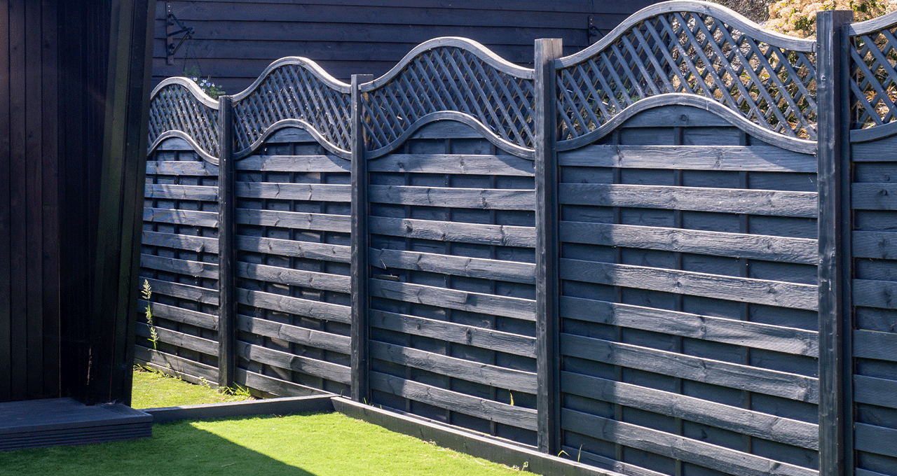 A painted type of wood fence. It is a dark, almost, black colour with a curved top.
