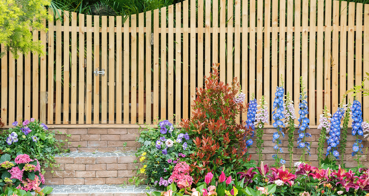 An image of a light wood garden fence with brick steps leading up to it.